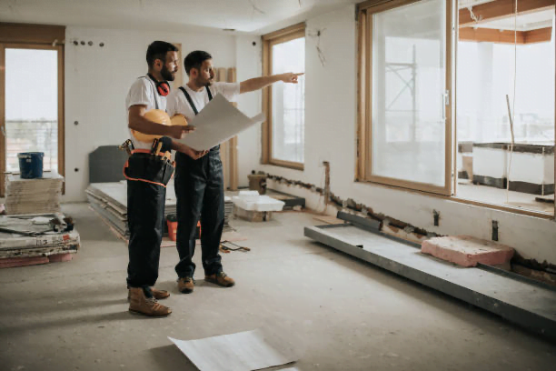 Two construction workers examining architectural plans and discussing the space-saving solutions for a modern interior design project.