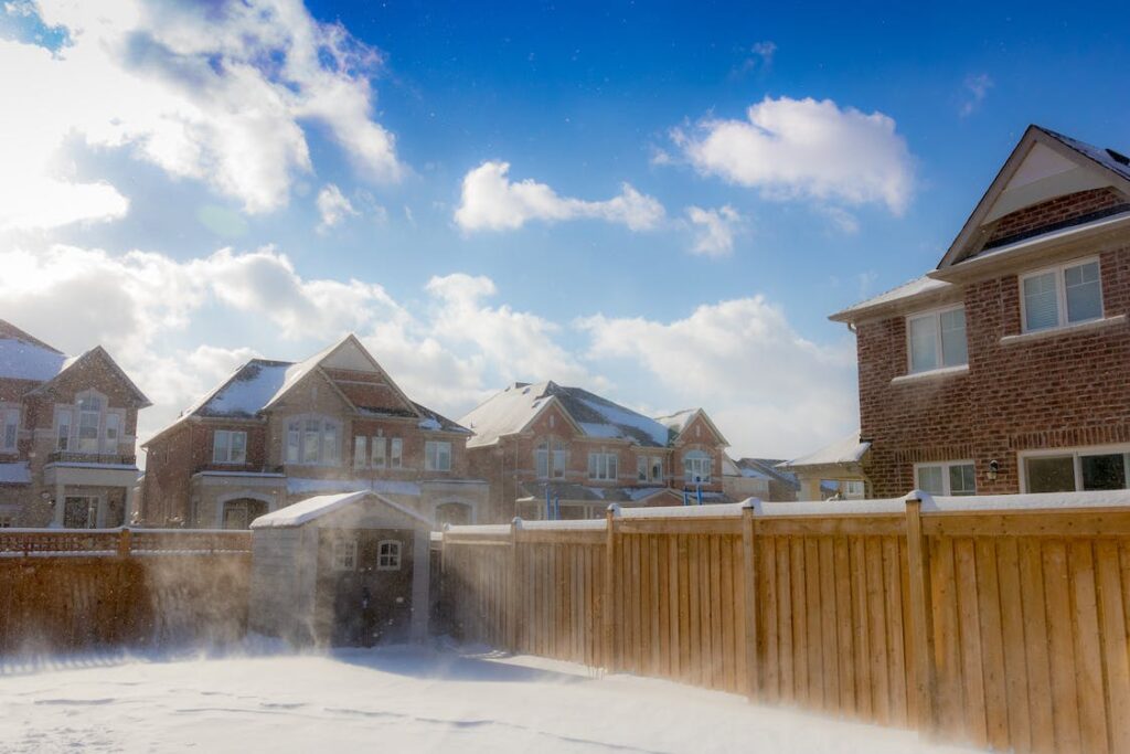 An elegant house with a light brown fence surrounding it, set against a beautiful blue sky with bright white clouds. A beautifully designed garden fence adhering to UK height regulations, providing privacy and enhancing the aesthetic appeal of the property.