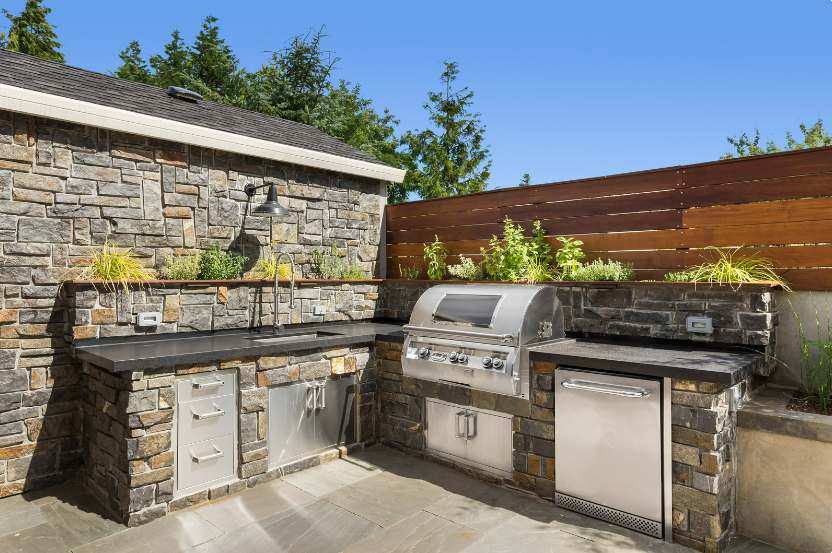 An image of a modern and stylish outdoor kitchen complete with a grill, sink, dining area, and lounge chairs, exemplifying Shear Architectural Design's expertise in creating outdoor spaces for entertaining.